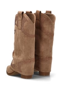 Botines de ante marrón con diseños recortados y acentos metálicos en el lateral, con un tacón bajo y refuerzo en la parte trasera para mayor durabilidad.