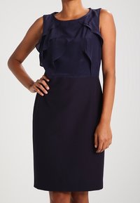 Robe sans manches bleu marine avec un haut froncé, tissu lisse, taille ajustée, ourlet au genou et un design simple et discret.