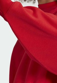 Rode sweatshirt met lange, brede mouwen en een hoge halslijn. Gladde textuur, lichte rekbaarheid van de stof en zichtbare naaddetails.