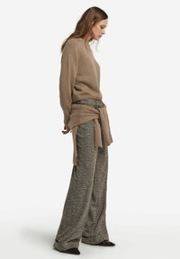 Beige gestrickter Pullover mit hohem Kragen, kombiniert mit strukturierten, weiten braunen Heringbone-Hosen. Der Pullover ist an der Taille gebunden.