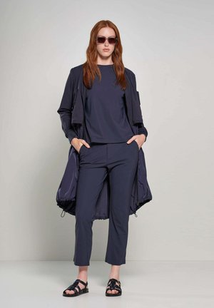 Navyblauw outfit bestaande uit een lange jas, een top met korte mouwen en tapse broek. Textuurstof met een minimalistisch design. Zwarte sandalen.
