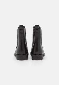 Zwarte nep leren enkellaarsjes met elastische zijpanelen, een gladde afwerking en stevige rubberen zolen. Voorzien van lusjes voor eenvoudig aan- en uittrekken.