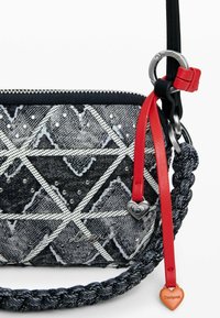 Farmer anyagú oldaltáska fekete-fehér geometriai mintával, ezüst szegecsekkel, piros díszítésekkel, fonott pánttal és ezüst színű fém kiegészítőkkel.