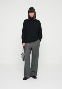 Maglione a collo alto a trecce nere, pantaloni larghi a righe grigie e una piccola borsa a fantasia. Texture morbide e vestibilità ampia.
