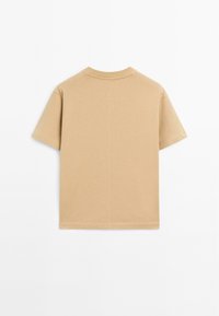 T-shirt in cotone beige con maniche corte, colletto tondo e taglio dritto. Presenta un design minimalista senza motivi o loghi visibili.
