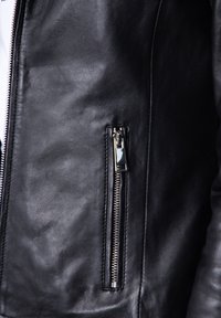 Black leather jacket close-up featuring a zippered pocket and smooth texture, with silver hardware accenting the design and functionality.