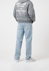 Grå huvtröja med vit text, ljusblå avslappnade jeans och grå sneakers. Slät tyg med en avslappnad design.