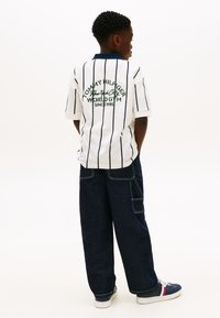 Λευκό κοντομάνικο πόλο μπλουζάκι με ναυτικά μπλε ρίγες και λογότυπο στην πλάτη, σε συνδυασμό με σκούρο τζιν παντελόνι cargo και ναυτικά μπλε αθλητικά παπούτσια.