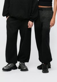 Μαύρη φόρμα με άνετη εφαρμογή και ελαστική μέση, συνδυασμένη με μαύρα chunky αθλητικά παπούτσια· λεία υφή και ελάχιστες λεπτομέρειες σχεδίασης.