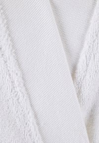 Châle blanc en tissu texturé, avec un côté présentant un matériau doux et pelucheux et l'autre un motif ribbé lisse.