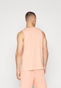 Sæt bestående af en ferskenfarvet tanktop og shorts, lavet af glat stof. Ærmeløs design med rund halsudskæring og afslappet pasform, velegnet til hverdag.
