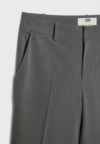 Pantalon gris foncé ajusté avec passants pour ceinture, poches latérales et un pli sur le devant, étiqueté STR Teen taille 38.