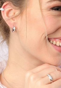Zilveren creolen met een gedraaide ontwerp, met kleine heldere edelstenen. Een zilveren ring met een edelsteenaccent is zichtbaar op de hand.