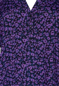 Chemise à motifs violets et noirs avec un col en V, une fermeture à boutons, et une texture lisse arborant un motif léopard.