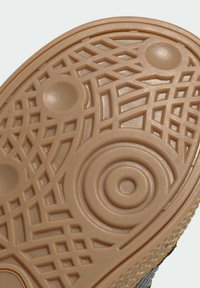 Suola di una scarpa con superficie in gomma beige testurizzata, caratterizzata da motivi circolari e geometrici per una migliore aderenza e stabilità.