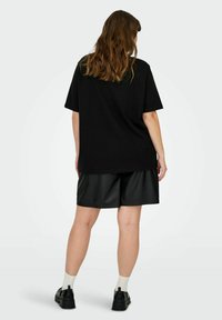 Camiseta negra de gran tamaño hecha de algodón, combinada con pantalones cortos de imitaciones de cuero negros. El fondo es blanco plano sin accesorios visibles.