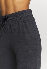Primer plano de pantalones deportivos de textura gris oscuro con cinturilla elástica y cordón en la cintura y área de la cadera de una persona.