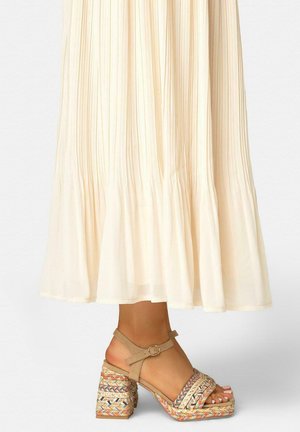 Sandalias beige con plataforma y correa en el tobillo, con detalles tejidos multicolores, combinadas con una falda plisada fluida en color crema.