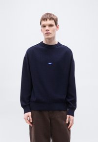 Μπλε πουλόβερ πλεκτό με στρογγυλή λαιμόκοψη με ριμπ και μανίκια με μανσέτες. Διαθέτει μικρό μπλε λογότυπο «HUGO» στο στήθος. Μαλακή υφή, άνετη εφαρμογή.