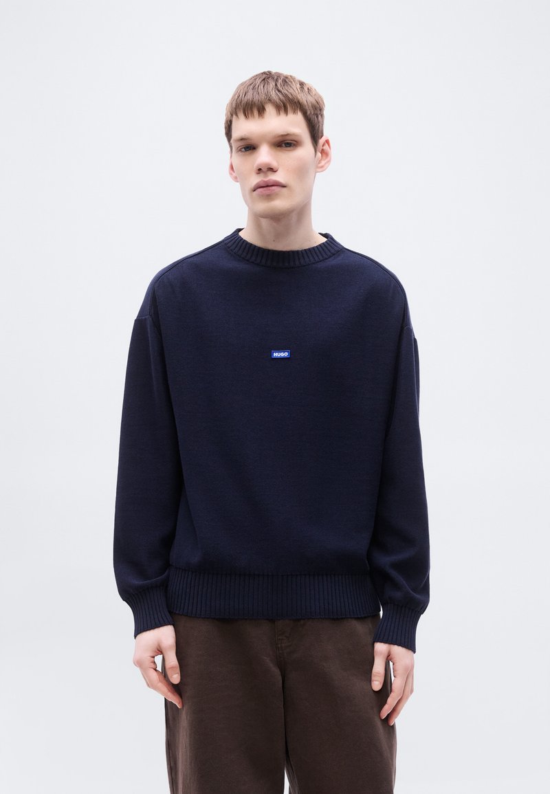 Μπλε πουλόβερ πλεκτό με στρογγυλή λαιμόκοψη με ριμπ και μανίκια με μανσέτες. Διαθέτει μικρό μπλε λογότυπο «HUGO» στο στήθος. Μαλακή υφή, άνετη εφαρμογή.