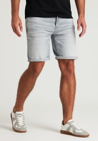 Shorts de mezclilla azul claro con dobladillos enrollados, que presentan detalles de desgaste. Combinados con zapatillas gris y blancas, atadas con una suela de goma marrón.