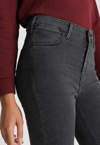 Vaqueros negros de mezclilla de cintura alta con un ajuste slim, con bolsillos frontales y costuras a tono, combinados con un sudadera color burdeos.