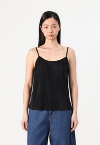 Camiseta negra plisada con tirantes finos, con una textura suave y un corte holgado, combinada con jeans de pierna ancha en azul.