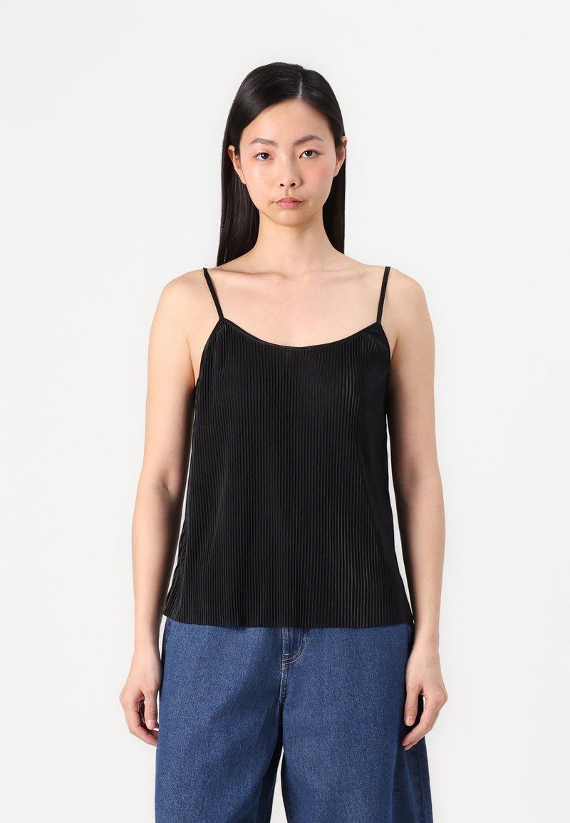 Camiseta negra plisada con tirantes finos, con una textura suave y un corte holgado, combinada con jeans de pierna ancha en azul.