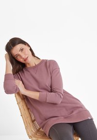 Oversized purple sweatshirt with long sleeves and ribbed cuffs, featuring a crew neckline and subtle stitching detail, worn over dark leggings.