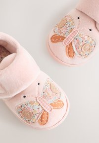 Bløde lyserøde babysutter med broderede sommerfugledesign, der indeholder blomster- og glitterdetaljer på en lys baggrund.