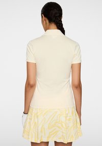 Koszulka polo w jasnym żółtym kolorze, z krótkimi rękawami i kołnierzykiem; zestawiona z białą spódnicą z żółtym abstrakcyjnym wzorem.