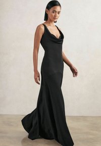 Černé šaty bez rukávů s volným výstřihem a přiléhavým korzetem, přecházející do rozšířené sukně. Hladká textura, minimalistický design bez vzorů.