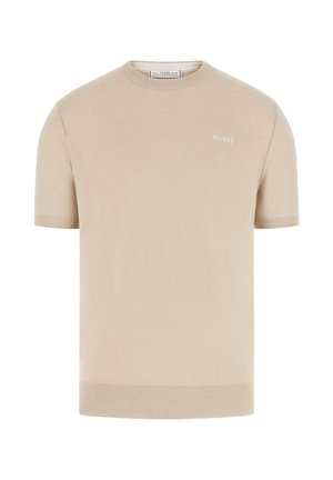 Beżowy krótki sweter z dzianiny z krótkim rękawem, okrągłym dekoltem i małym białym logo "GUESS" na górnej lewej stronie klatki piersiowej.