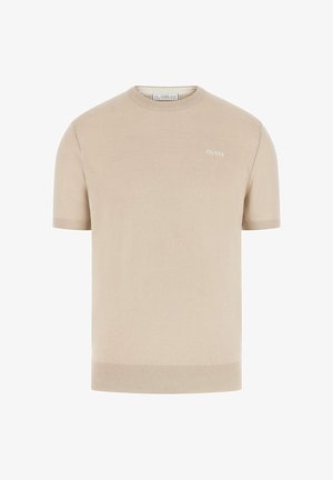 Beżowy krótki sweter z dzianiny z krótkim rękawem, okrągłym dekoltem i małym białym logo "GUESS" na górnej lewej stronie klatki piersiowej.