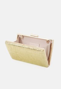 Kopertówka z metalowym zapięciem w kolorze złotym, z teksturowanym żółtym materiałem zewnętrznym, gładką podszewką i ustrukturyzowanym kształtem. Widoczna wewnętrzna kieszeń.