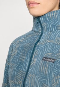 Fleecejacke in Blau mit Wellenmuster. Ausgestattet mit hohem Kragen, durchgehendem Reißverschluss und Columbia-Logo-Tag auf der linken Brust.