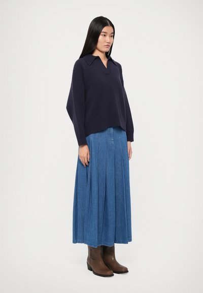 Navy knit polo sweater with a collar, paired with a pleated denim skirt. The model wears brown ankle boots, showcasing a casual ensemble.