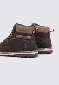 Botas altas de cuero marrón con collar de color beige, bucles en el talón de color rojo-blanco-azul, ojales de metal y suela a rayas en blanco, azul y rojo.