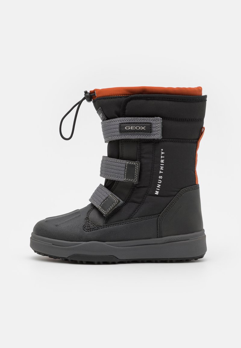 Bota de invierno negra aislada con parte superior naranja, que cuenta con tres correas de Velcro grises, tejido texturizado y una suela de goma diseñada para tracción.