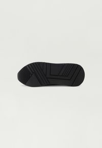 Melnas gumijas kurpes zole ar teksturētu saķeri, kurai ir horizontālas un diagonālas rievas, lai nodrošinātu vilkmi, un "GUESS" zīmols sānos.