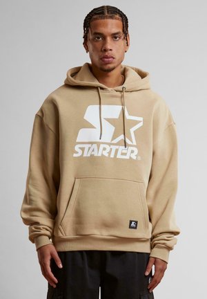 Beige hoodie crafted from cotton blend, featuring a large white "Starter" logo with star, drawstring hood, and front pocket.