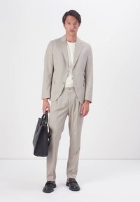 Lys grå dress med slank passform, ensidig blazer, matchende bukser og en hvit T-skjorte med rund hals; holder en svart skinnveske.