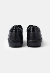 Black leather shoes with a glossy toe, stitched detailing along the sides, and a low, cushioned sole. Round shape with a relaxed fit.