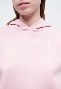Rozā džemperis ar mīkstu audumu, kuram uz krūtīm ir balts izšūts Jumpman logotips. Kapuci ir apvilkusi ribota apdare papildu detaļai.