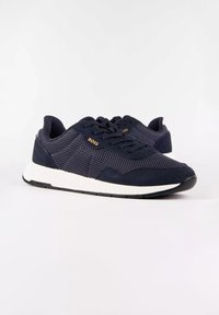 Baskets en mesh et en daim bleu marine avec semelles blanches et semelles extérieures noires, dotées de lacets noirs et d'un logo doré "BOSS" sur le côté.