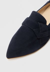 Σουέντ μοκασίνι σε ναυτικό μπλε με μυτερή μύτη, που διαθέτει διακοσμητικό διπλωμένο λουράκι στο πάνω μέρος και λείο καφέ πέλμα.