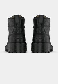 Stivaletti in pelle nera con superficie strutturata, suole spesse e marchio discreto. Presentano una linguetta per tirare e dettagli in metallo sui talloni.