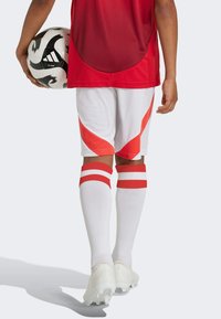 Röd atletisk tröja, vita shorts med röda detaljer och ränder, vita strumpor med röda ränder och vita fotbollsskor. Håller i en svart och vit fotboll.