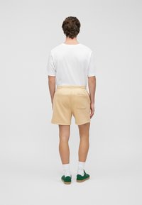 Μπέζ σορτς από φούτερ με πίσω τσέπη, φορεμένα με λευκό μπλουζάκι και πράσινα παπούτσια. Διαθέτουν απαλό ύφασμα και ελαστική μέση.