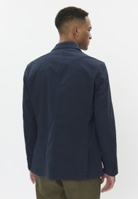 Blazer in cotone blu navy, design strutturato, monopetto con spacchetto posteriore, cuciture minime e quattro dettagli con bottoni sulle maniche.